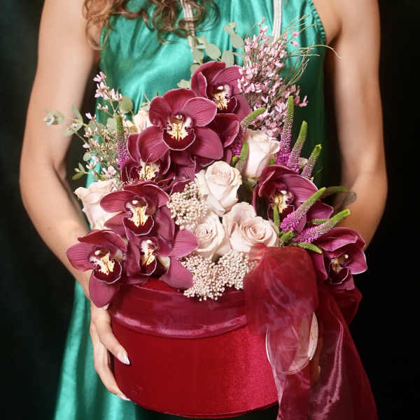 Bouquet of burgundy orchids and pale pink roses in a red hatbox