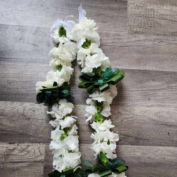 White carnation lei with green ribbon bows on a wood surface
