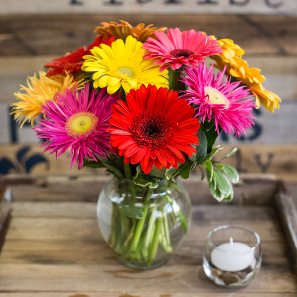 Colorful gerbera daisies in a glass vase with a small candle nearby