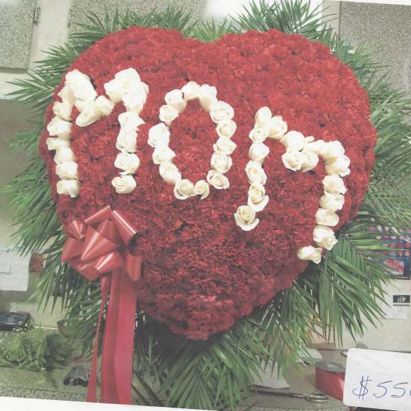 Heart-shaped red floral tribute with white rose lettering and a red ribbon bow