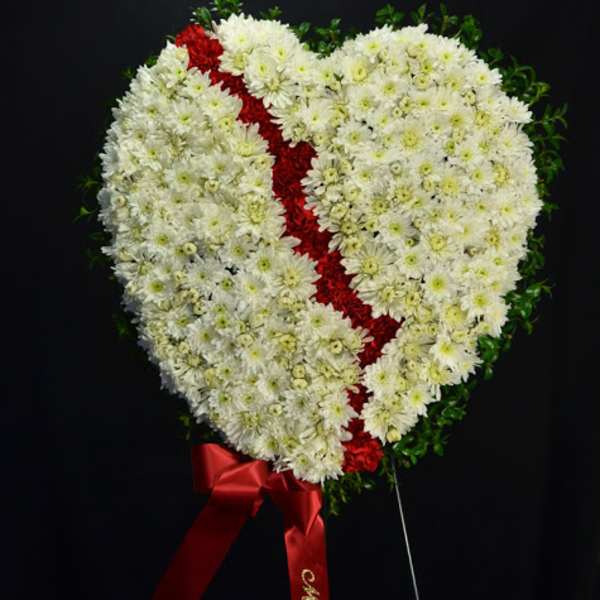 Heart-shaped white floral wreath with a red ribbon accent on a black background