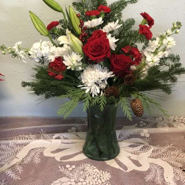 Red roses and white flowers in a green glass vase with pine accents