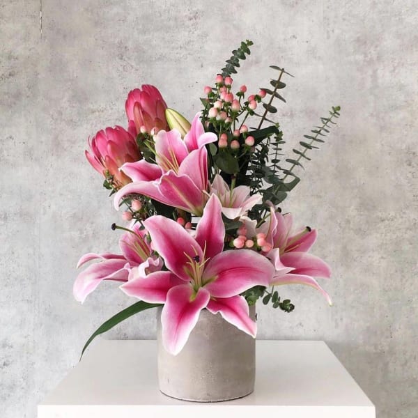 Pink lilies arranged in a white vase with eucalyptus and berry accents