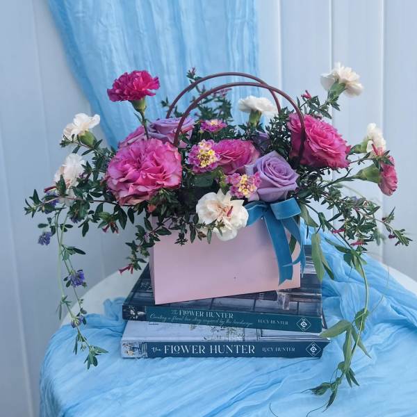 Pink and lavender roses with small white blooms in a pink box with a blue ribbon
