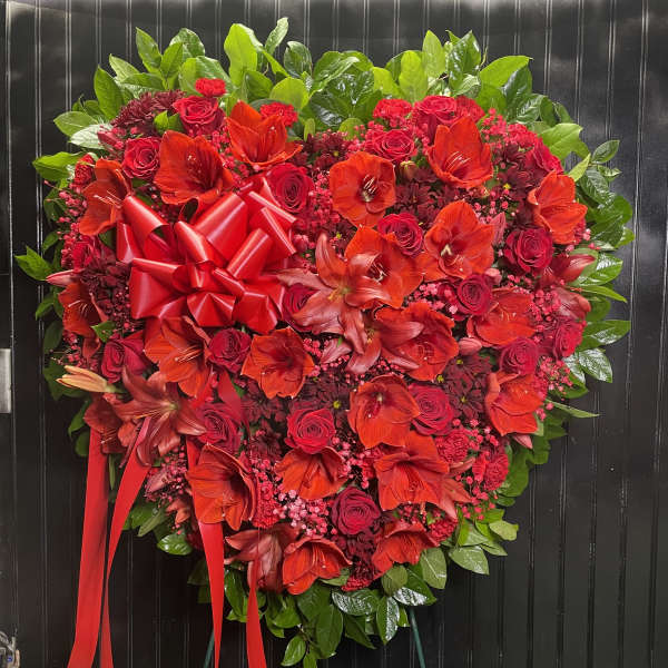 Heart-shaped red floral wreath with a ribbon bow on a stand