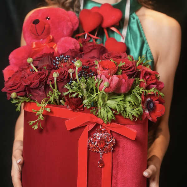 Red roses and poppies in a red gift box with a teddy bear and heart decorations