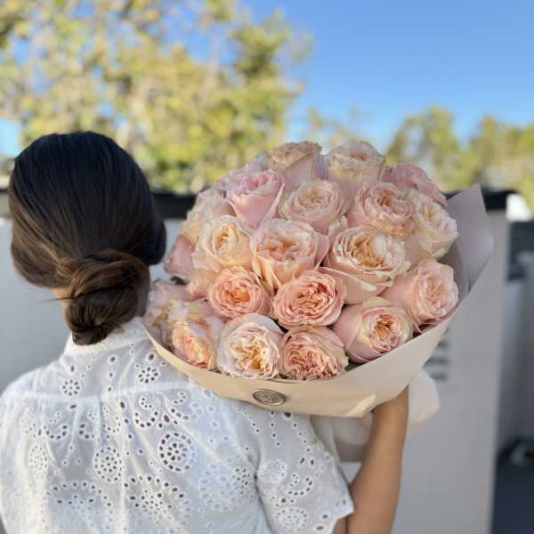 Woman holding a bouquet of pale pink roses wrapped in beige paper