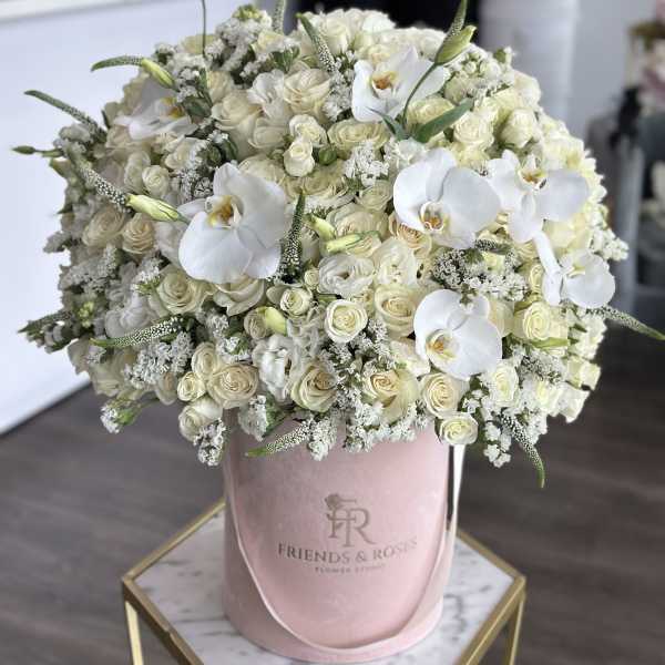 White roses and orchids arranged in a pink hatbox