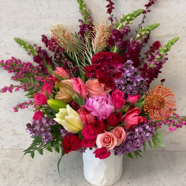 Large mixed bouquet in a white vase with pink, red, purple, and peach flowers