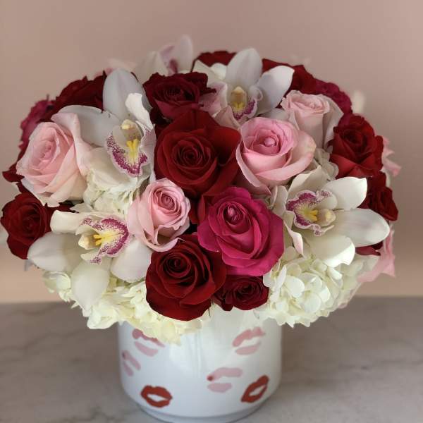 Bouquet of red and pink roses with white orchids in a white vase