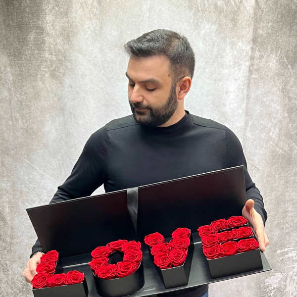 Man holding a black box arrangement spelling LOVE with red roses