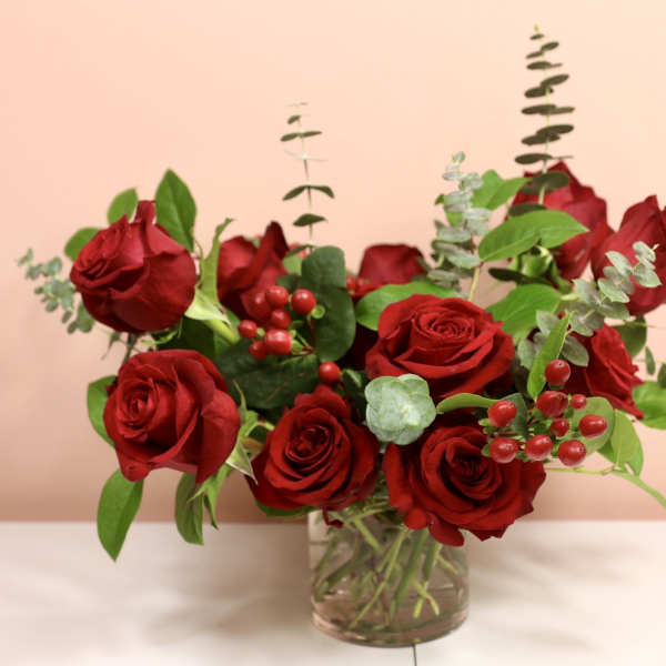 Red roses arranged in a clear glass vase with berries and greenery