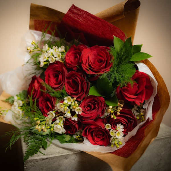 Bouquet of red roses with white filler flowers wrapped in brown and red paper