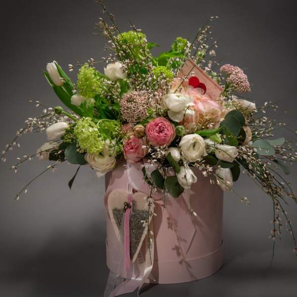 Pink and white floral arrangement in a pink hatbox with a ribbon and heart tag