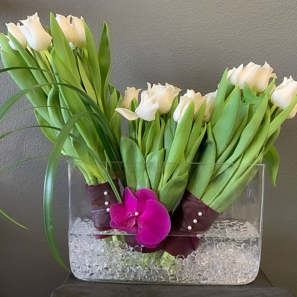 White tulips in a clear rectangular vase with a purple orchid accent