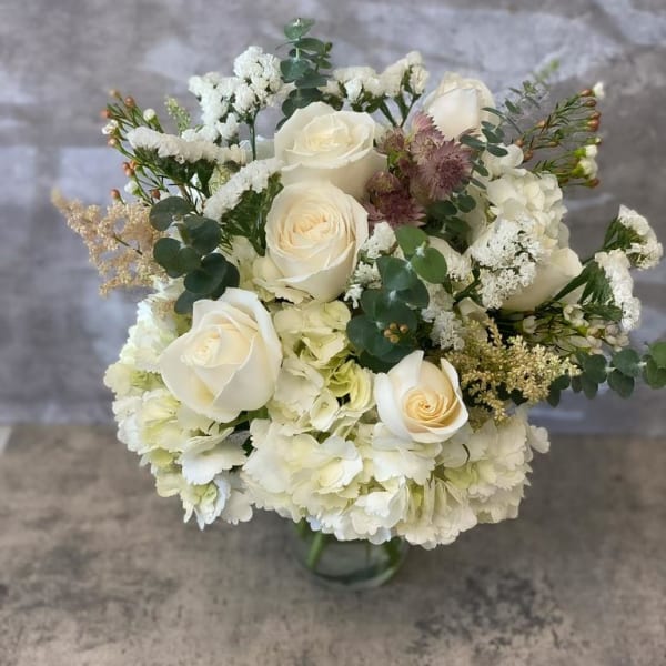 White rose bouquet with hydrangeas and greenery in a glass vase