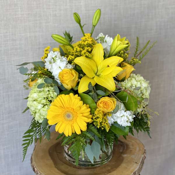 Yellow lilies and roses arranged with white blooms in a glass vase