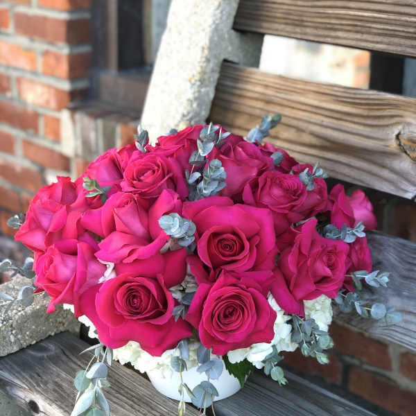 Hot pink rose bouquet in a white container with blue-gray foliage
