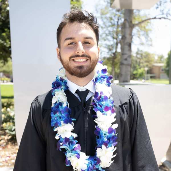 Man in graduation gown wearing a blue and white flower lei