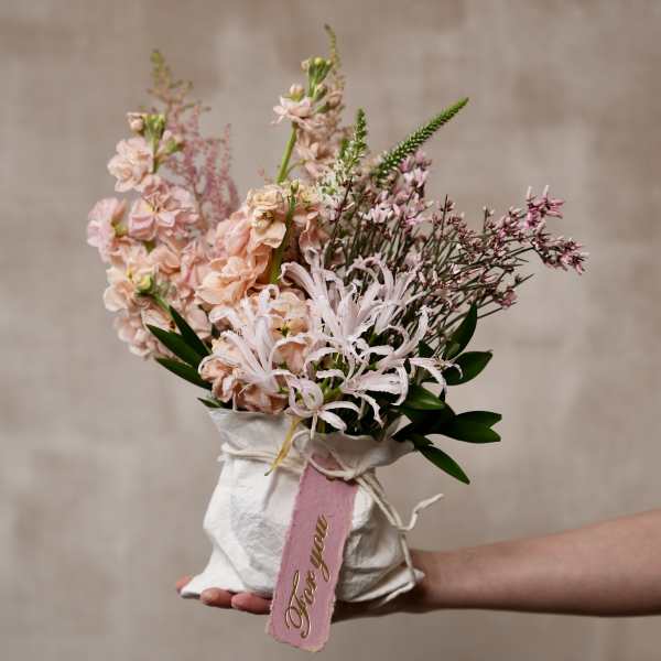 Handheld bouquet of pale pink flowers wrapped in white paper