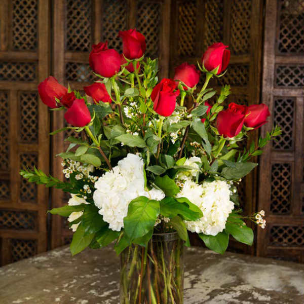 Red roses and white hydrangeas arranged in a clear glass vase.