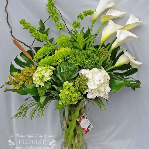 Green and white floral arrangement in a clear glass vase with calla lilies
