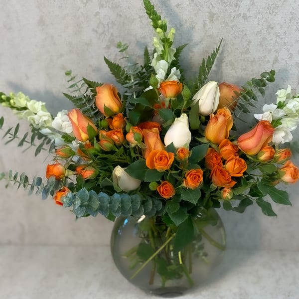 Orange and white rose bouquet in a round glass vase