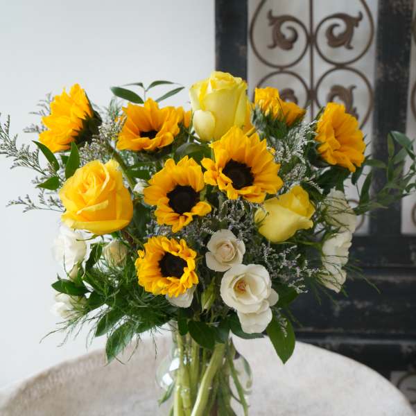Yellow roses and sunflowers arranged in a clear glass vase