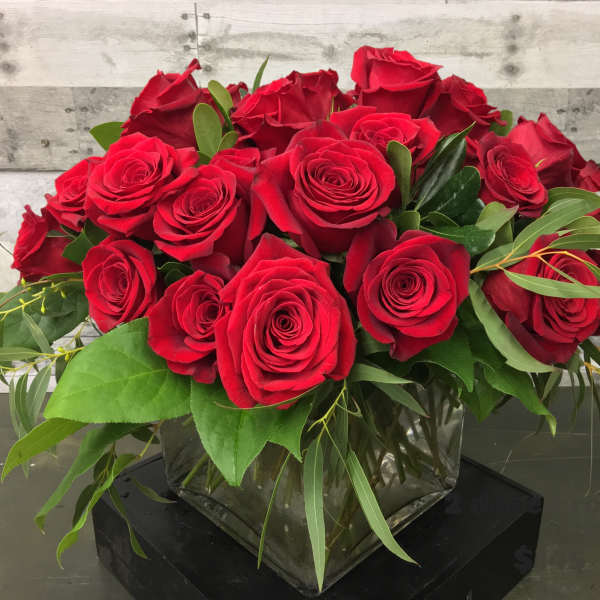 Red roses arranged in a clear square vase with greenery