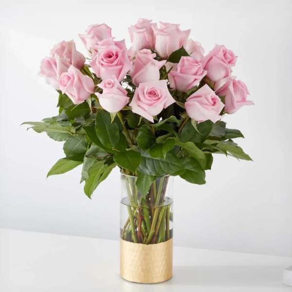 Pink roses arranged in a clear glass vase with a gold base