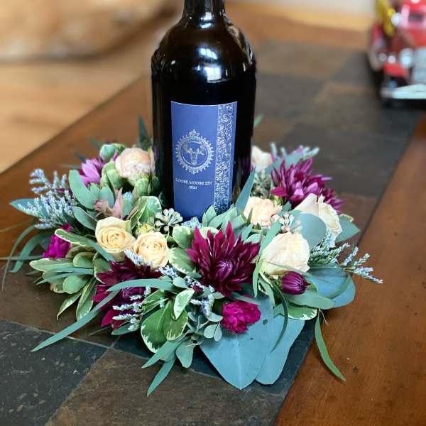 Wine bottle surrounded by a floral wreath of cream and purple flowers