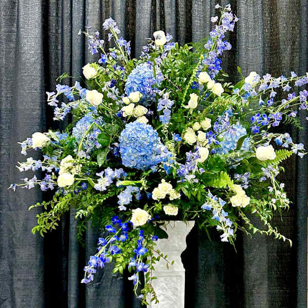 Tall blue and white floral arrangement in a white pedestal vase