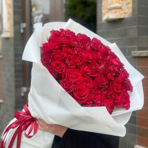 Large bouquet of red roses wrapped in white paper with a red ribbon