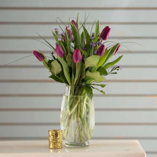 Pink tulips in a clear glass vase with a small gold candle holder