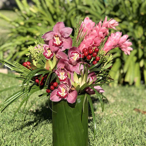 Pink orchids arranged in a tall green vase with red berry accents