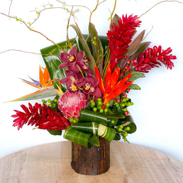 Tropical flower arrangement with red and orange blooms in a wooden vase