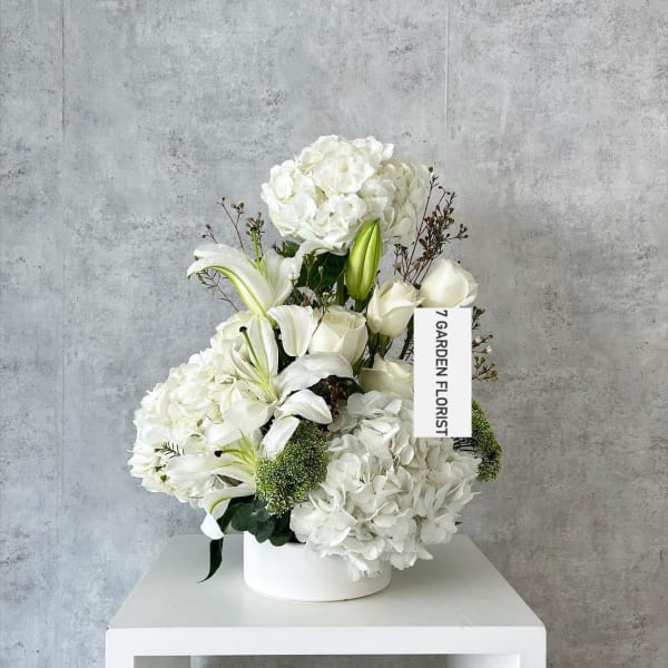 White floral arrangement in a round white box with lilies and hydrangeas