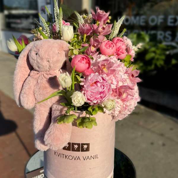 Pink flower arrangement with a plush bunny in a round box