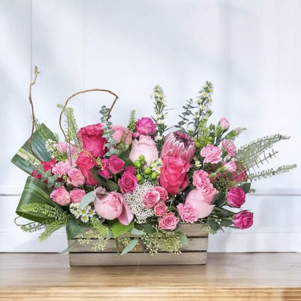 Pink rose and protea arrangement in a wooden box