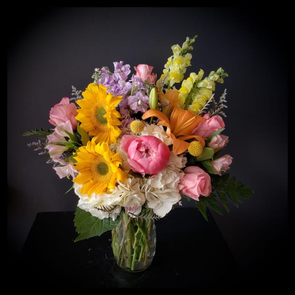 Colorful bouquet with sunflowers, pink roses, and lilies in a glass vase