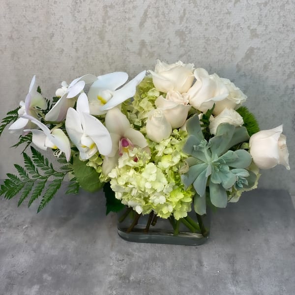 White orchids and roses arranged in a glass vase with pale green hydrangeas