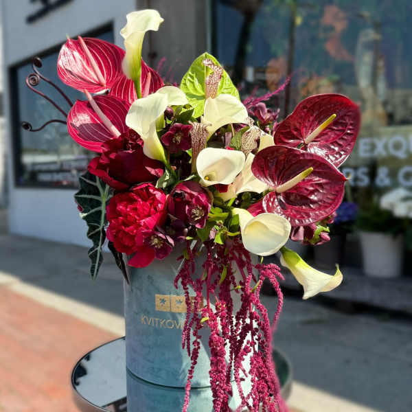 Bouquet of red anthuriums, white calla lilies, and dark burgundy blooms in a blue hatbox