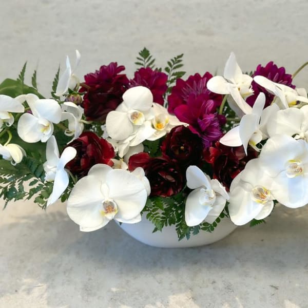 White orchids and dark red flowers arranged in a white bowl vase
