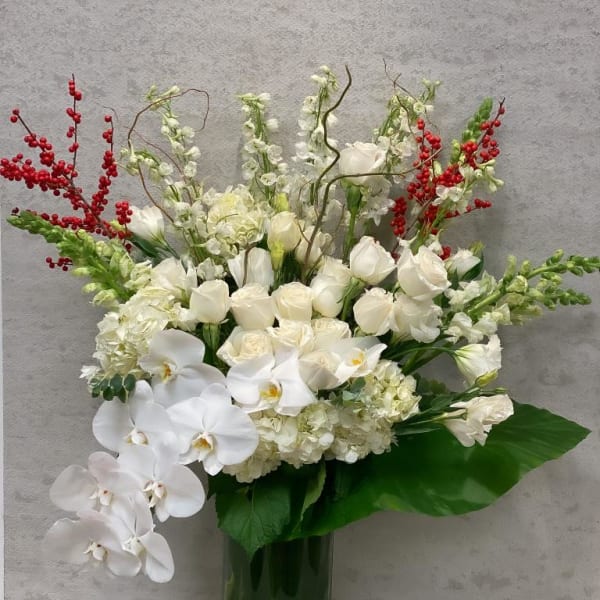 White floral arrangement in a tall green glass vase with red berry accents