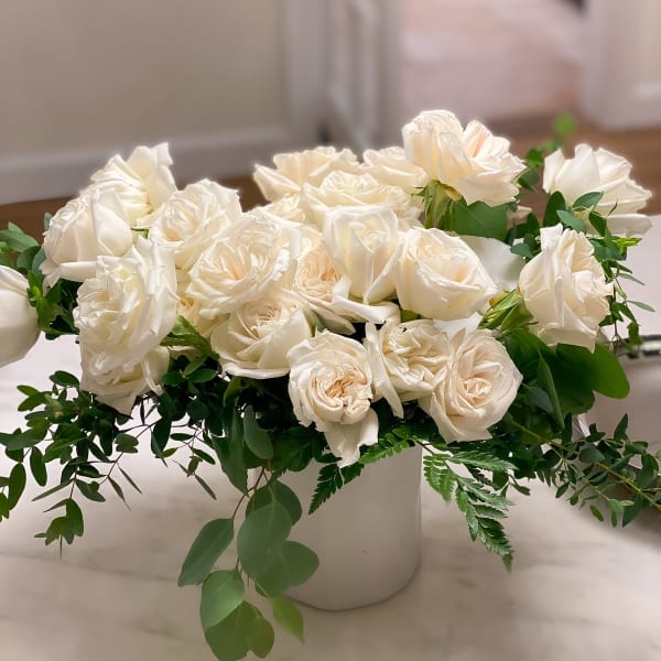 White rose arrangement in a white vase with greenery