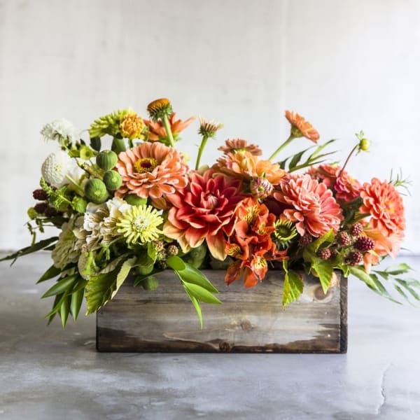 Low floral arrangement of orange and peach blooms in a wooden box