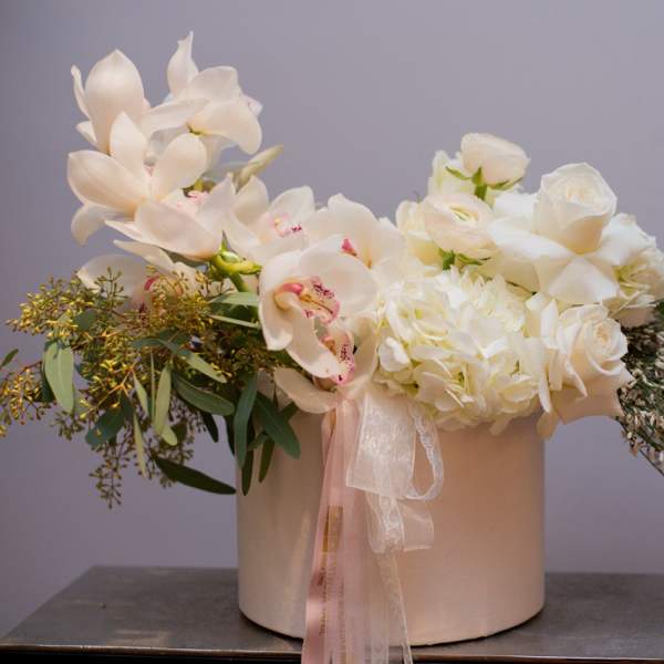 White floral arrangement in a round box with orchids and roses