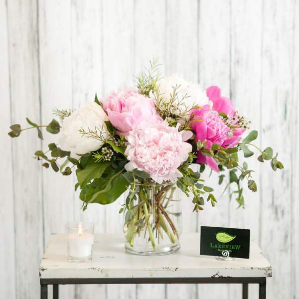 Pink and white peonies in a clear glass vase with greenery