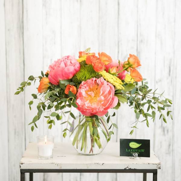 Pink and orange floral arrangement in a clear glass vase with a candle beside it
