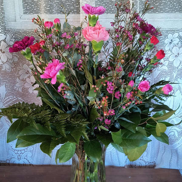 Pink and purple carnations in a clear glass vase with mixed greenery